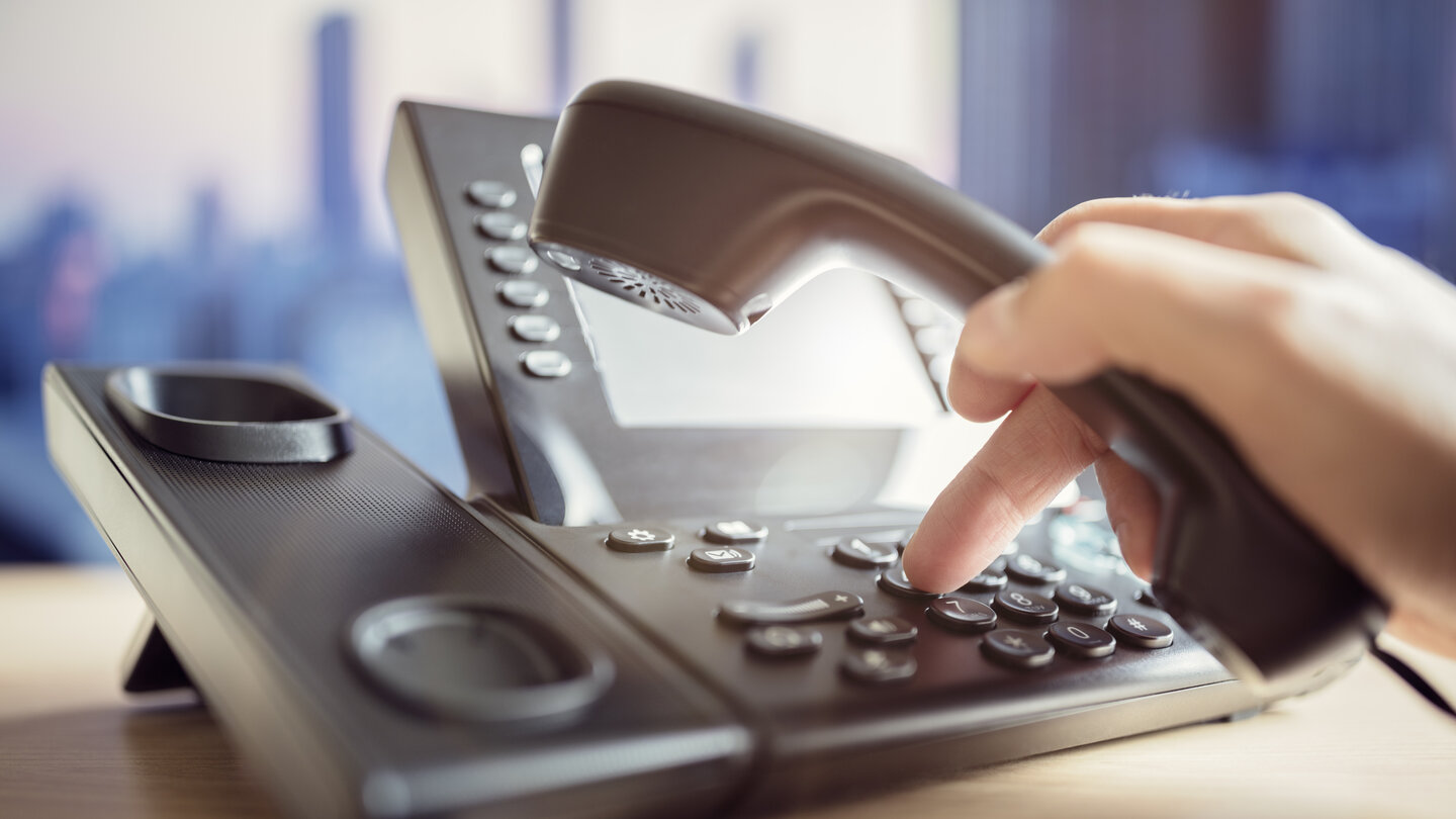 Eine Person wählt eine Nummer auf dem Festnetztelefon von Green