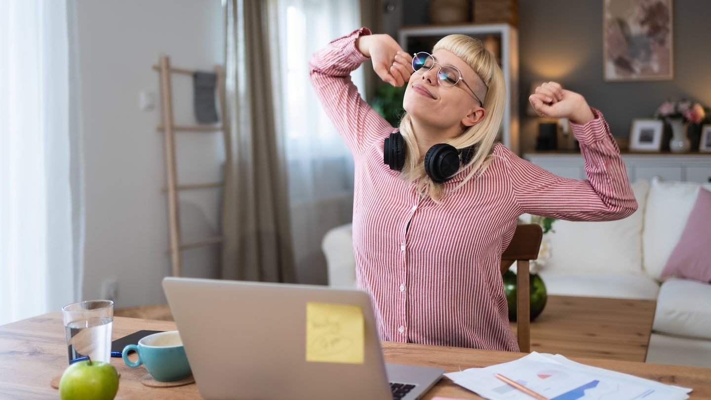 A woman at her desk in front of a laptop stretches and relaxes comfortably