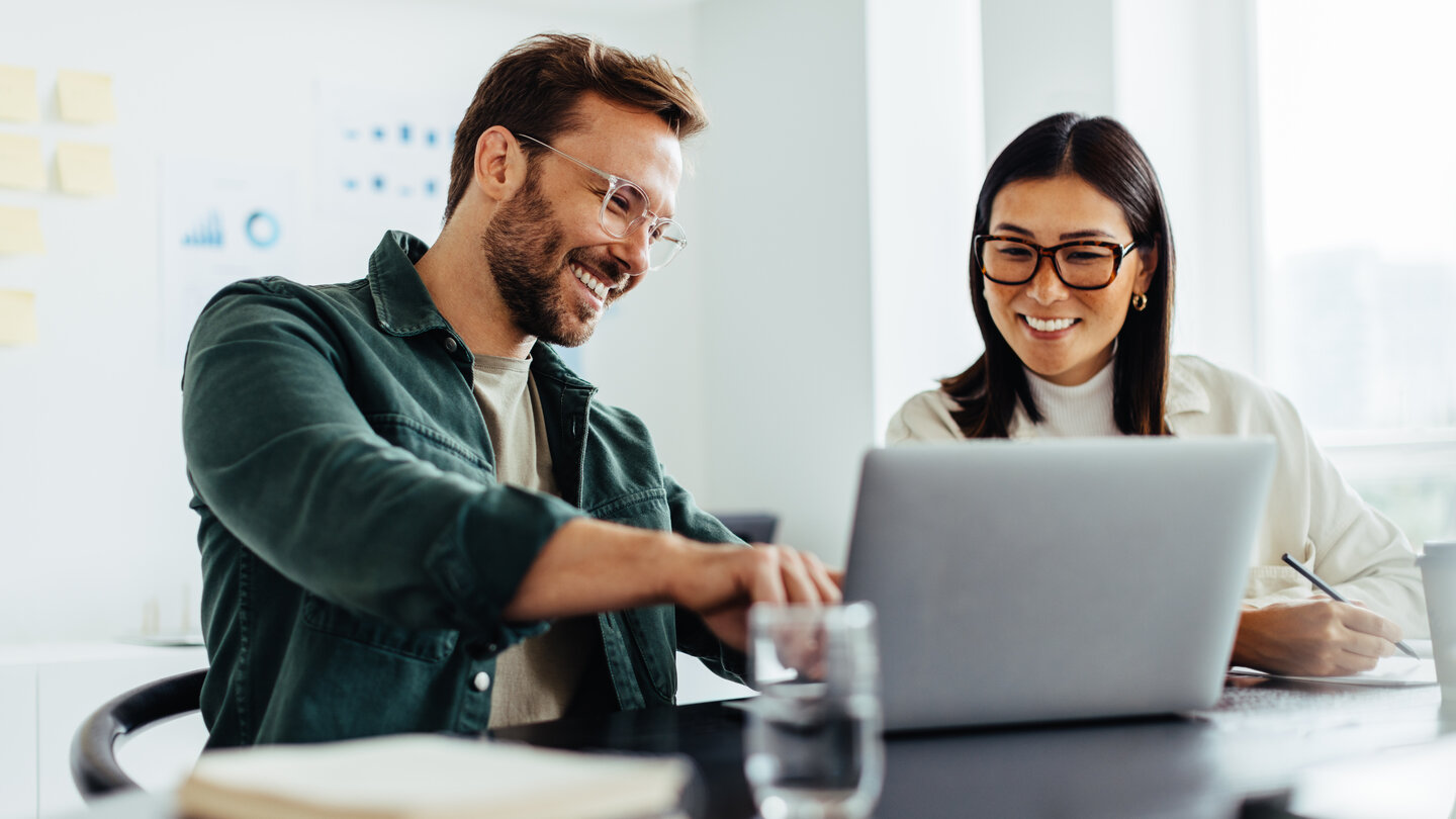 Mann und Frau besprechen etwas und zeigen dabei auf Laptop