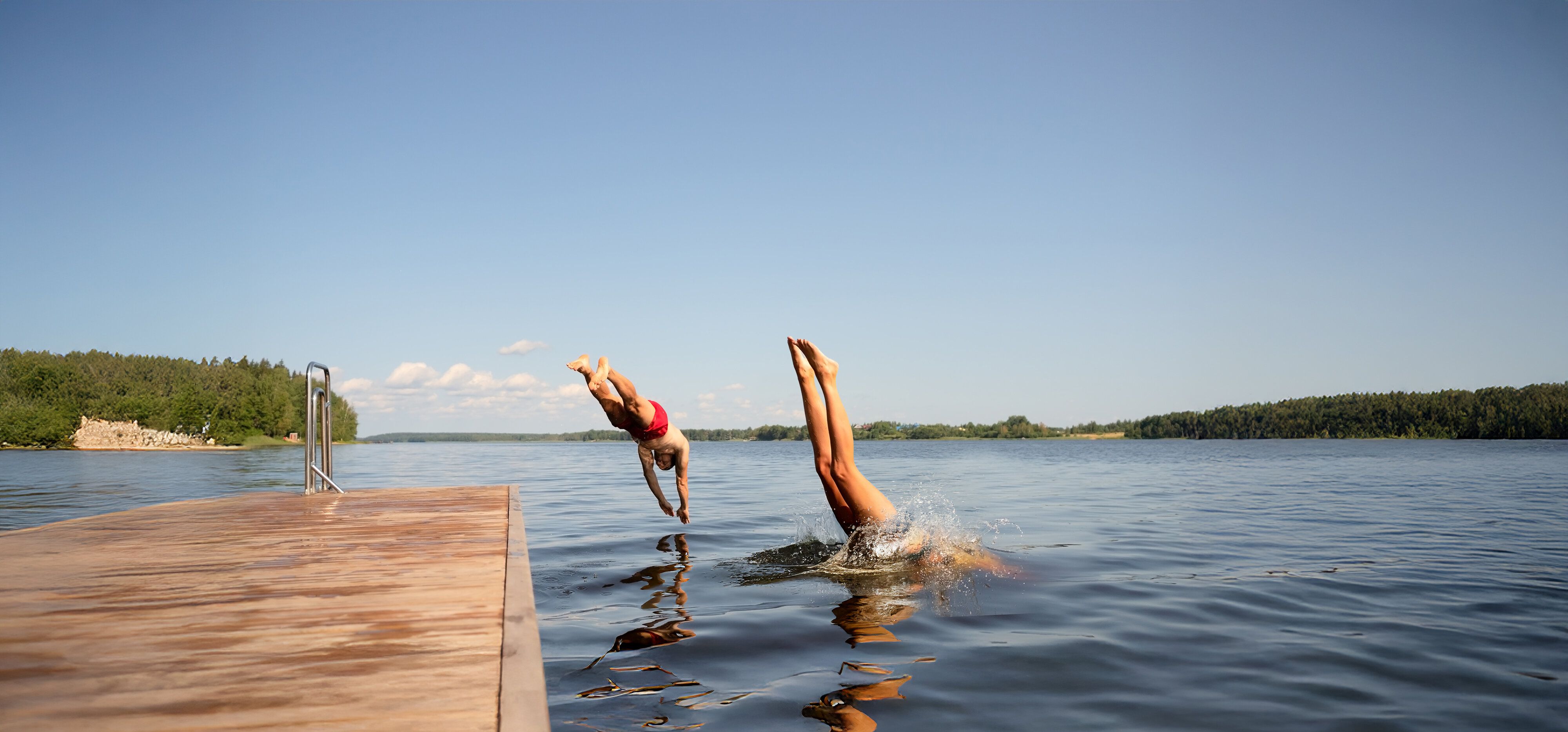 Zwei Menschen springen kopfüber gleichzeitig von einem Steg in einen See an einem sonnigen Sommertag