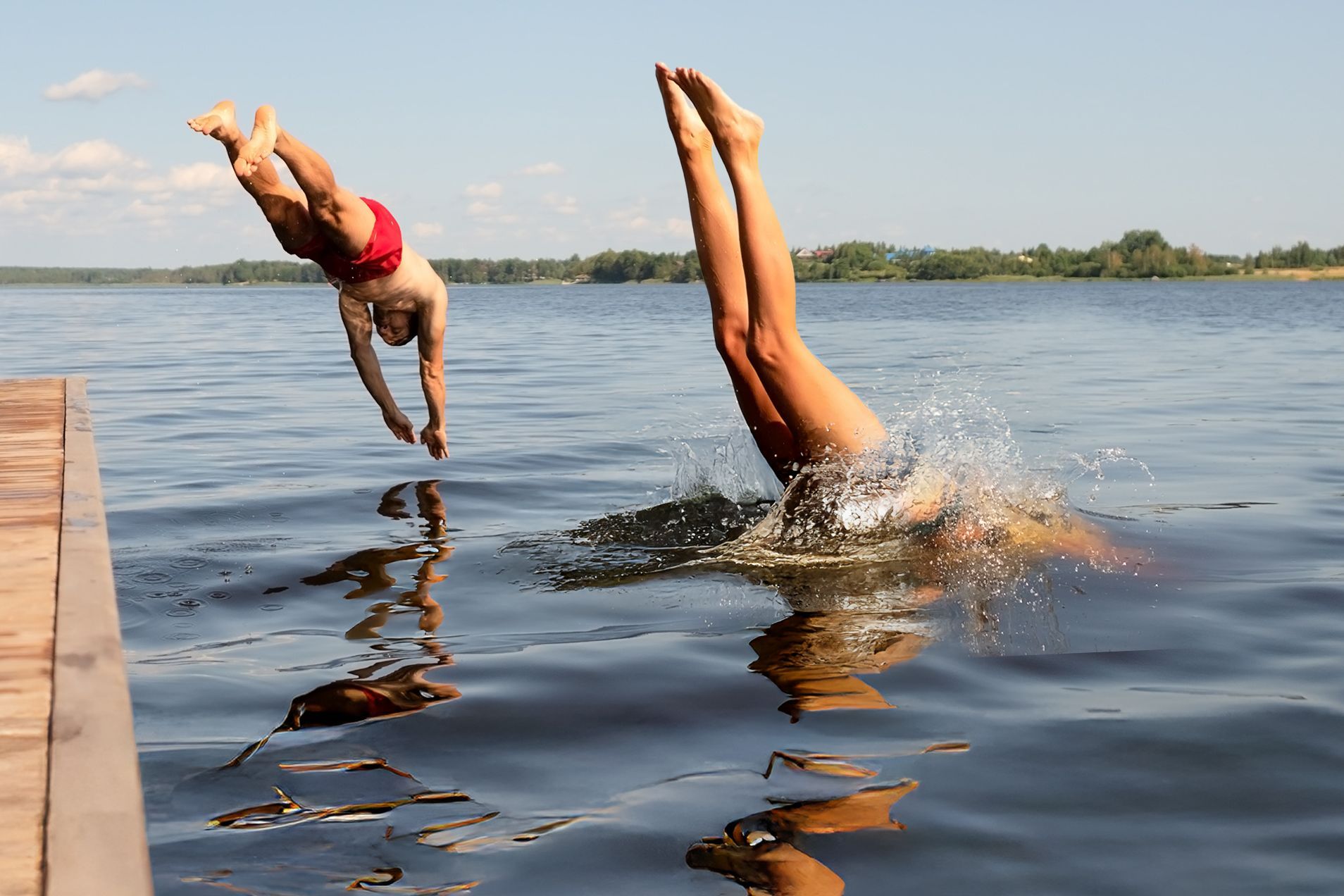 Zwei Menschen springen kopfüber gleichzeitig von einem Steg in einen See an einem sonnigen Sommertag