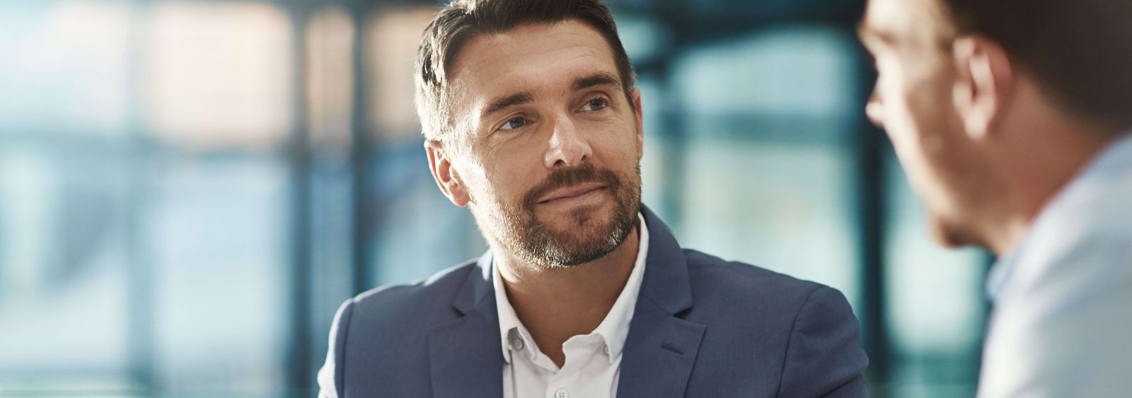 Man in a suit listens to another man while talking